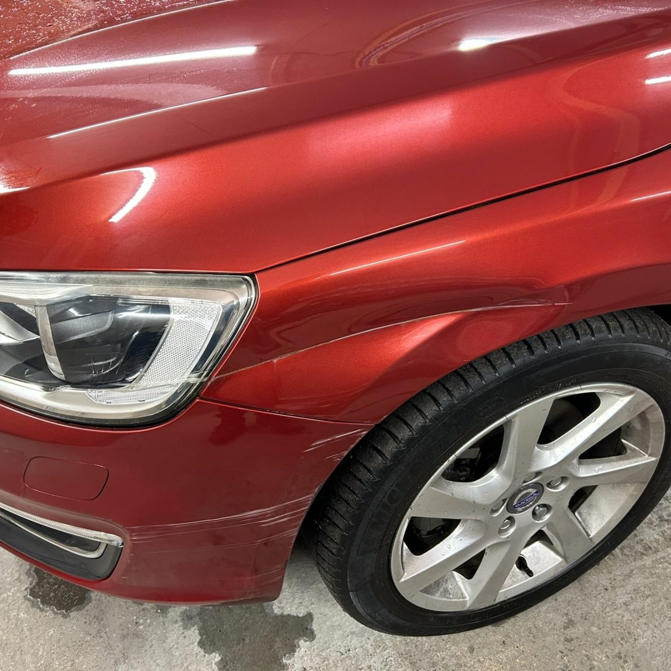Red car with a scratched front panel and a silver alloy wheel.